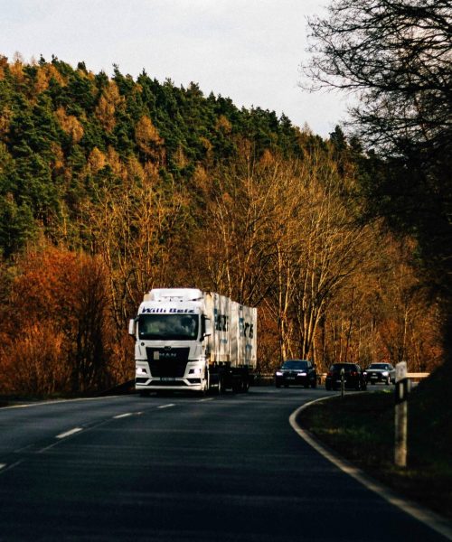 A truck drives on a scenic winding road surrounded by autumn foliage and forest.